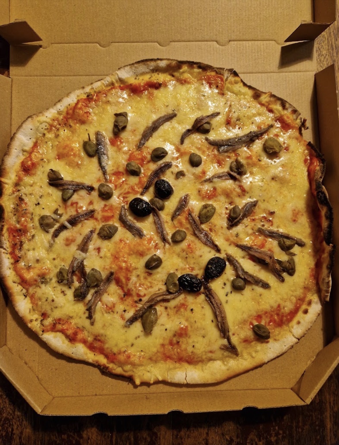 Pizza anchois, câpres et olives sortie du four à bois
